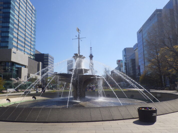 青空の中で西4丁目の噴水が光に反射している画像