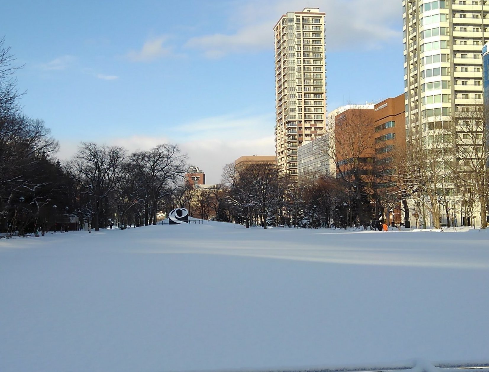 青空で遠くにブラックスライドマントラが見える足あとが無い雪の大通公園西8丁目の画像