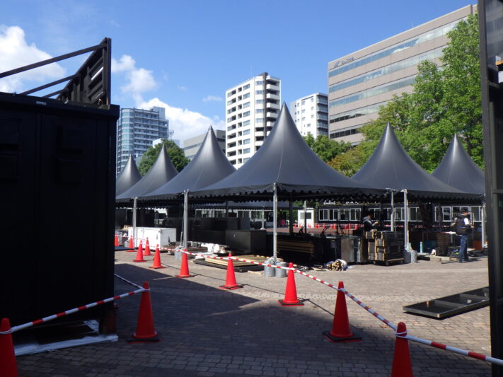 先がとがった黒いテントが三角コーンやポールで囲われたオータムフェスト設営の画像 