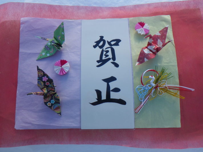 賀正の筆文字の周りを折り鶴や水引で飾っている画像