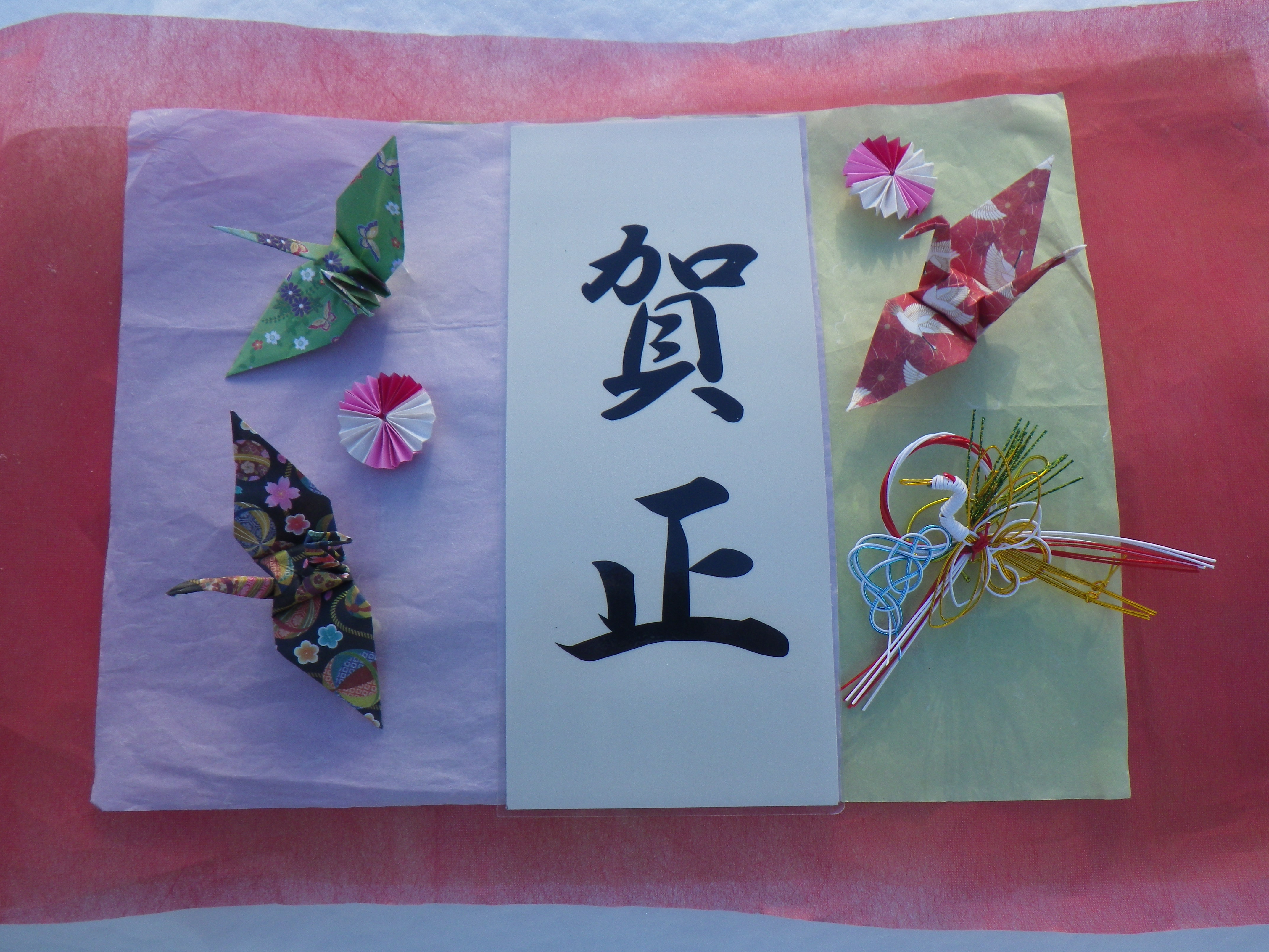 賀正の筆文字の周りを折り鶴や水引で飾っている画像